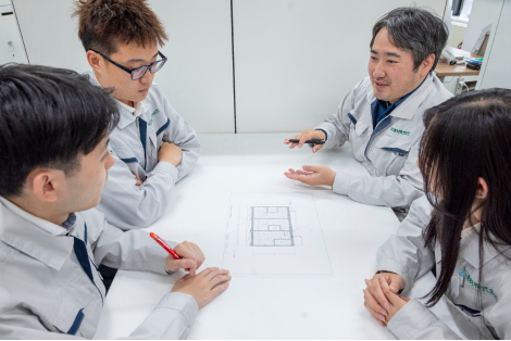図面を前に向かい合って打ち合わせをする作業着のスタッフ4名